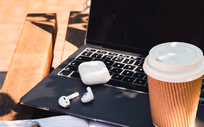 AirPods, a coffee cup and a laptop on a sunny outdoor desk